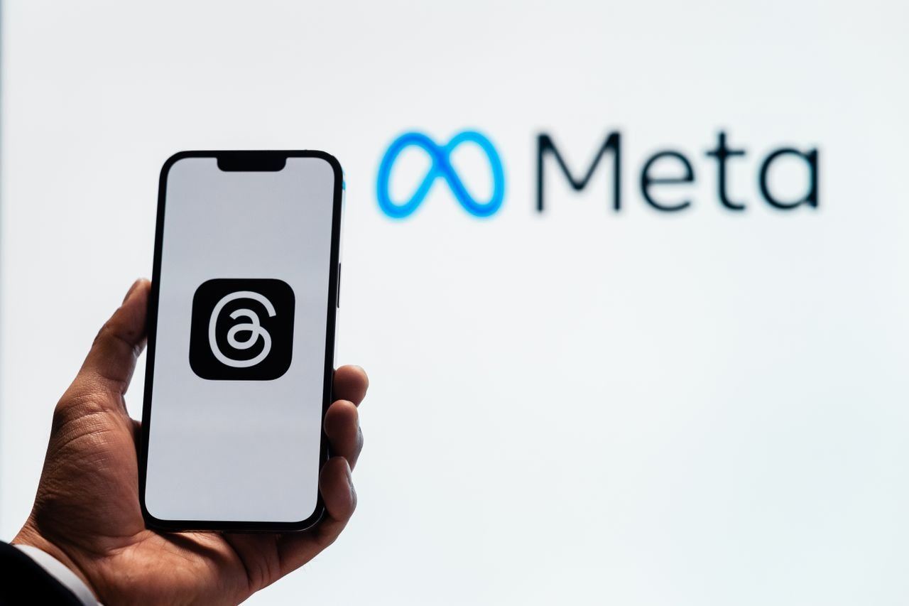 services-03 A hand holding a smartphone showing the Threads app with Meta logo in the background.