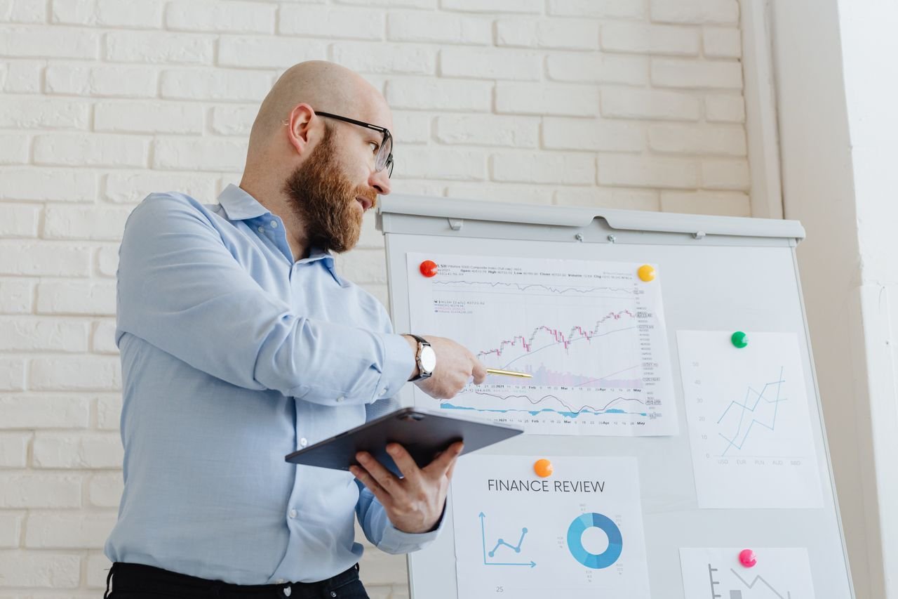 The Art of Drawing Readers In: Your attractive post title goes here Man giving a business presentation with financial graphs on a whiteboard using a tablet for explanation.